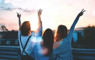 Three people stand side by side facing a sunset, arms raised joyfully in the air. Their silhouettes are highlighted by the sun, creating a carefree and celebratory moment—perfect for carousel teasers capturing joyful memories.
