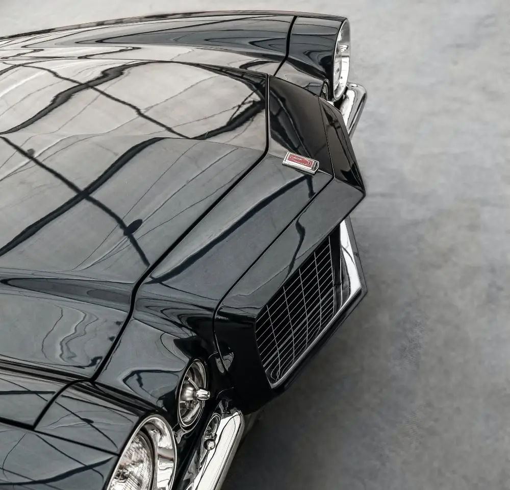 Close-up of the front bonnet and grille of a classic black Chevrolet Camaro, its badge and headlamps visible, reflecting the geometric shapes of a large window above—a perfect example for American classic car insurance enthusiasts.