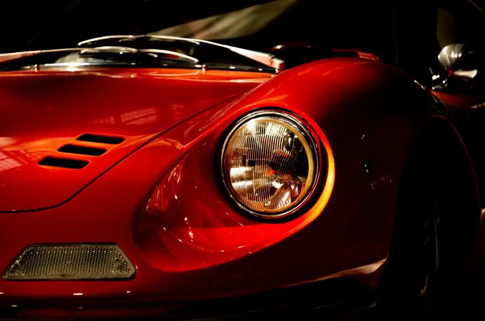 Close-up of the front of a classic red Ferrari sports car, focusing on the round headlamp, curved bonnet, and sleek aerodynamic lines under dramatic lighting—perfect for showcasing your Ferrari Insurance needs.