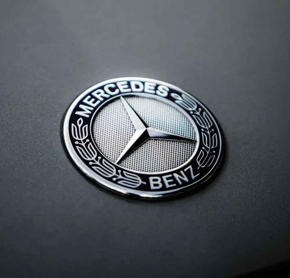 Close-up of a silver Mercedes-Benz emblem with a three-pointed star inside a circle, set against a smooth dark background. The words Mercedes-Benz appear around the edge—an image perfect for discussing Mercedes-Benz Insurance.
