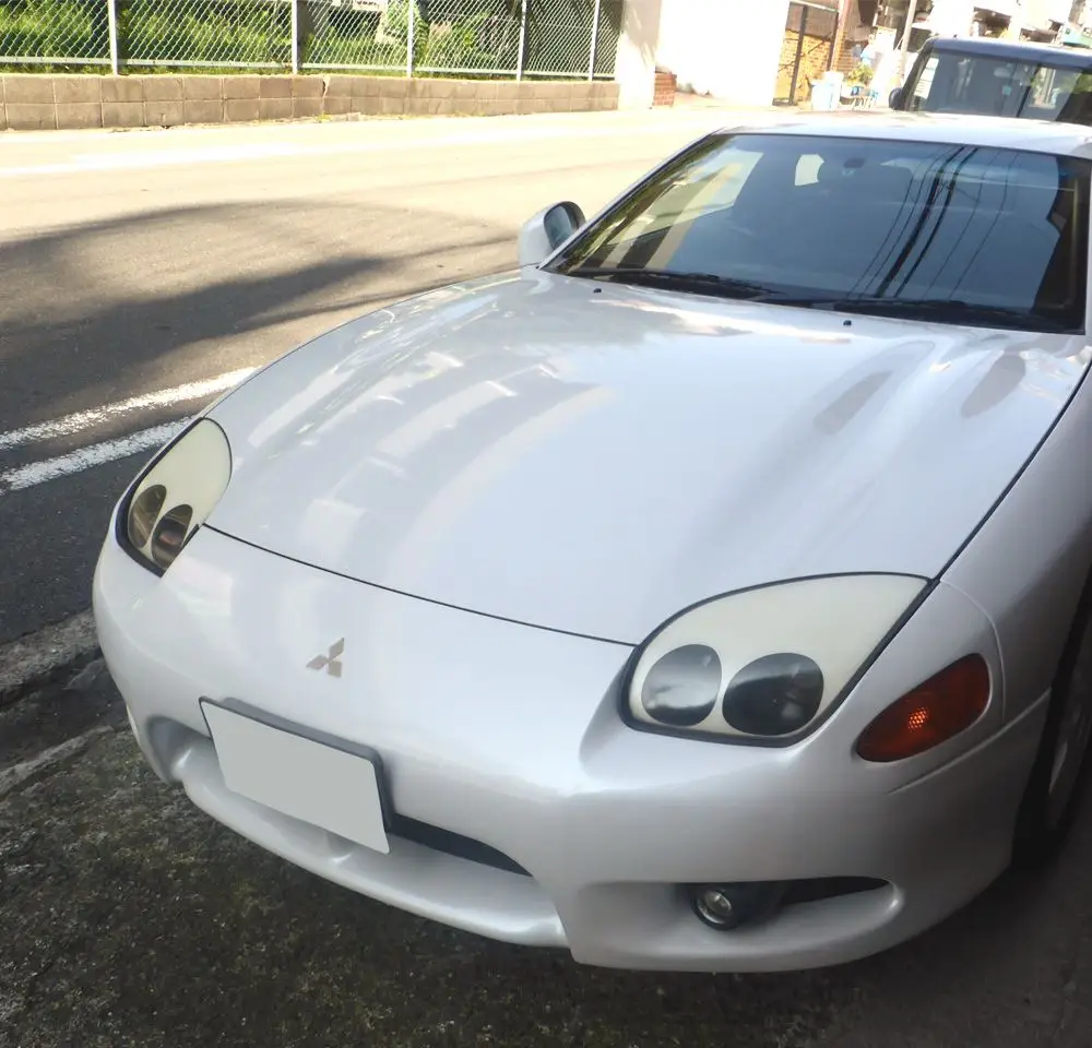 A white Mitsubishi 3000GT sports car, also known as the Mitsubishi GTO, is parked near a kerb on a sunny day, with its front end and pop-up headlamps clearly visible—perfect for those considering Mitsubishi car insurance.