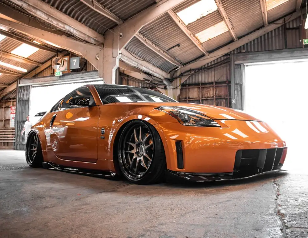 A low-angle view of a Nissan sports car with black wheels and a lowered body kit, parked inside an industrial warehouse with exposed beams and large doors—a striking scene that emphasises the importance of the right car insurance.