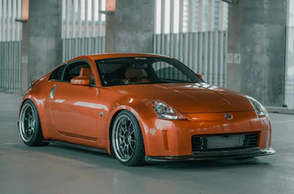 An orange Nissan 350Z sports car with custom wheels is parked indoors in a modern concrete parking structure with large windows, perfectly capturing the style that makes 350Z Insurance essential for dedicated owners.