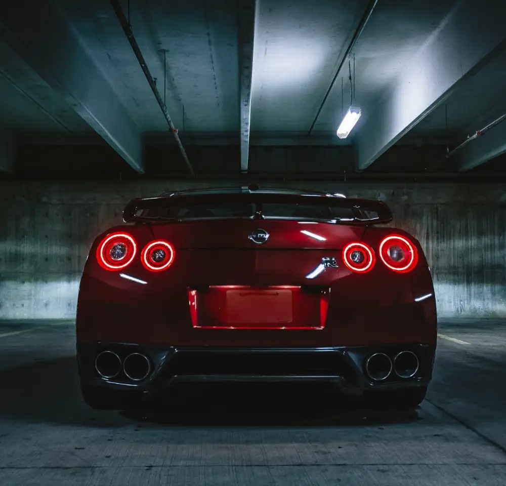 A red Nissan 350Z with circular red tail lights is parked in a dimly lit concrete garage, viewed from the rear—a striking sight for anyone considering Nissan 350Z insurance.