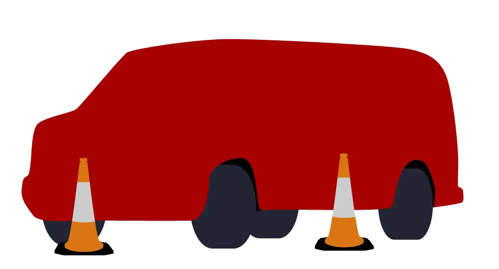 A red van with missing wheels is resting on its axles, with two orange traffic cones placed near its front and rear.