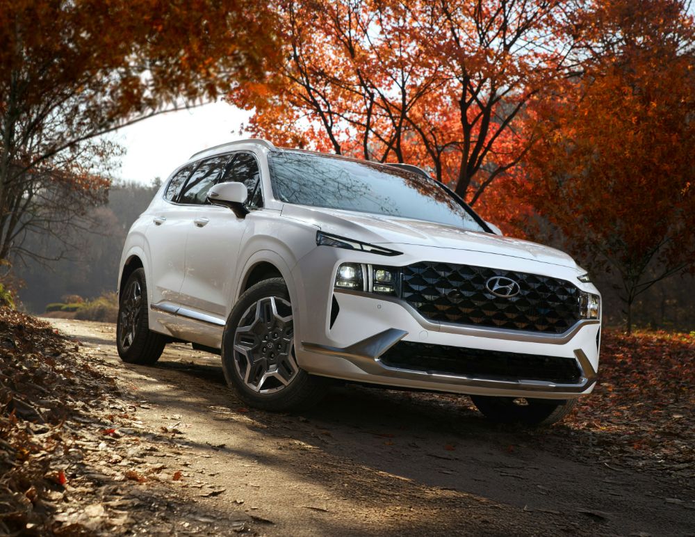 Hyundai SUV is parked on a winding dirt path framed by vibrant autumn foliage. The vehicle is angled to highlight its bold front grille, sleek headlights, and sculpted alloy wheels.